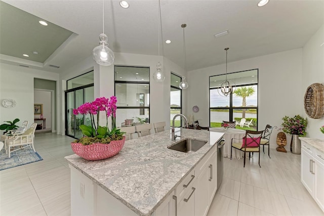 kitchen featuring a sink, decorative light fixtures, a kitchen island with sink, and white cabinetry