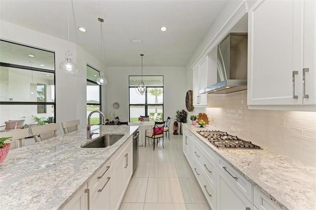 kitchen with tasteful backsplash, wall chimney range hood, white cabinets, stainless steel appliances, and a sink