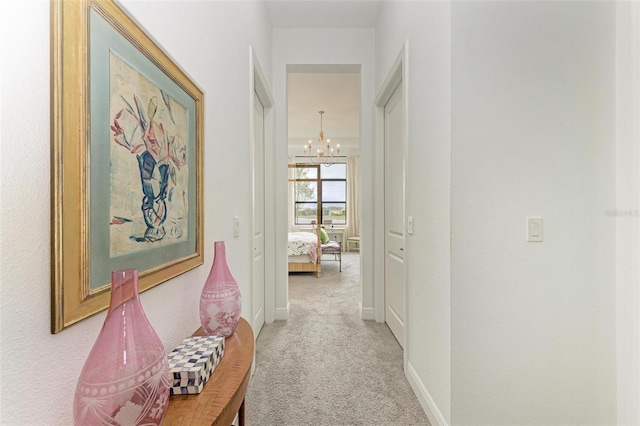 hallway with light colored carpet, baseboards, and an inviting chandelier