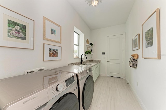 clothes washing area with sink, washing machine and dryer, and cabinets