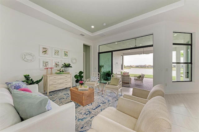 living room featuring tile patterned floors, a water view, a raised ceiling, recessed lighting, and baseboards