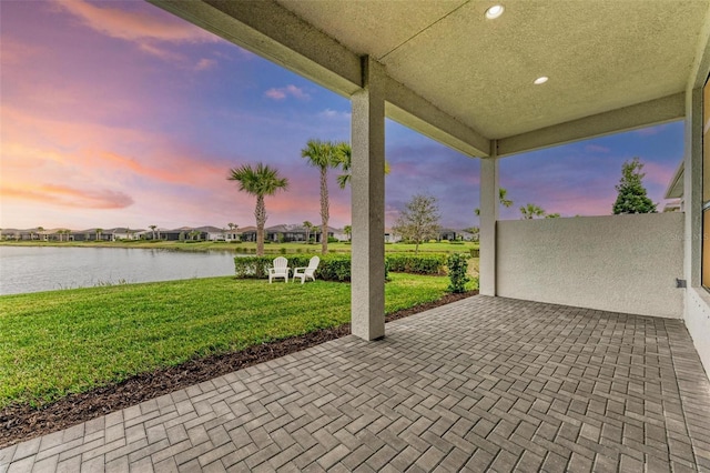 patio terrace at dusk with a water view and a lawn