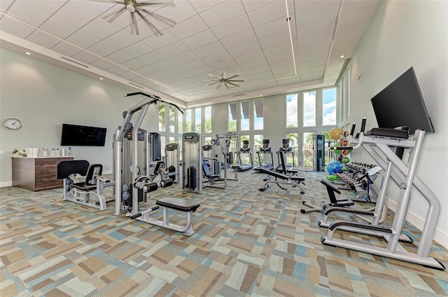 gym featuring a towering ceiling, a ceiling fan, baseboards, and carpet floors