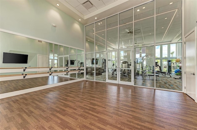 gym featuring expansive windows, recessed lighting, french doors, a towering ceiling, and wood finished floors