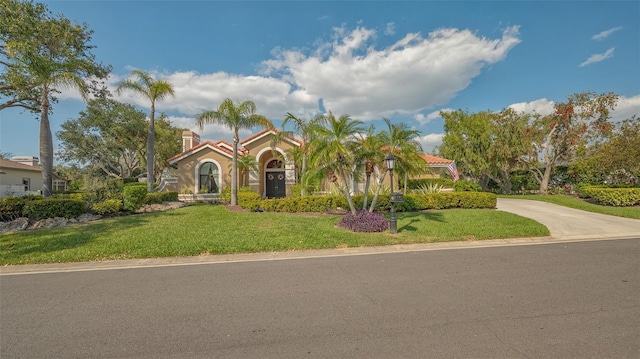 mediterranean / spanish-style home with driveway, a front lawn, and a tiled roof