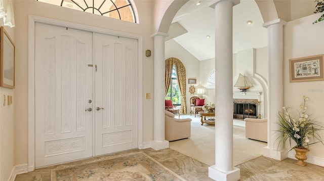 carpeted foyer entrance with ornate columns, a lit fireplace, high vaulted ceiling, and arched walkways