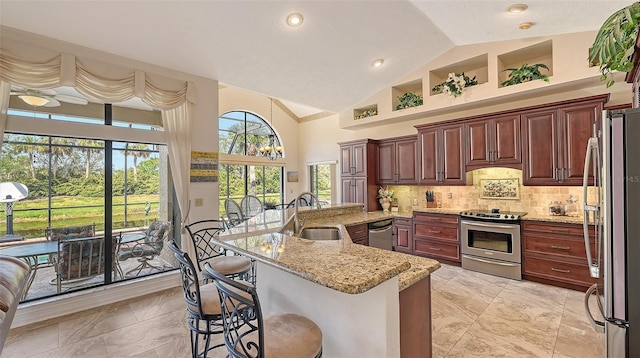 kitchen with light stone countertops, stainless steel appliances, a sink, a kitchen breakfast bar, and decorative backsplash