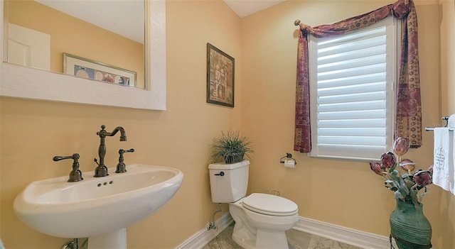 half bath with toilet, baseboards, and a sink