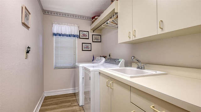 laundry area with light wood finished floors, cabinet space, a sink, independent washer and dryer, and baseboards