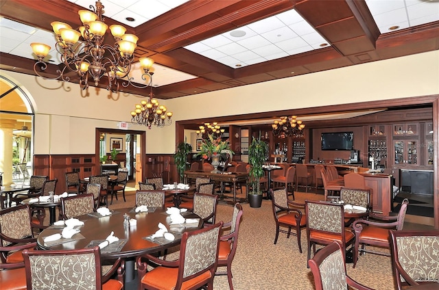 carpeted dining space with a wainscoted wall, a chandelier, and beam ceiling