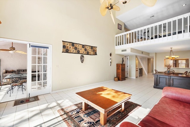 tiled living room with ceiling fan with notable chandelier and a high ceiling