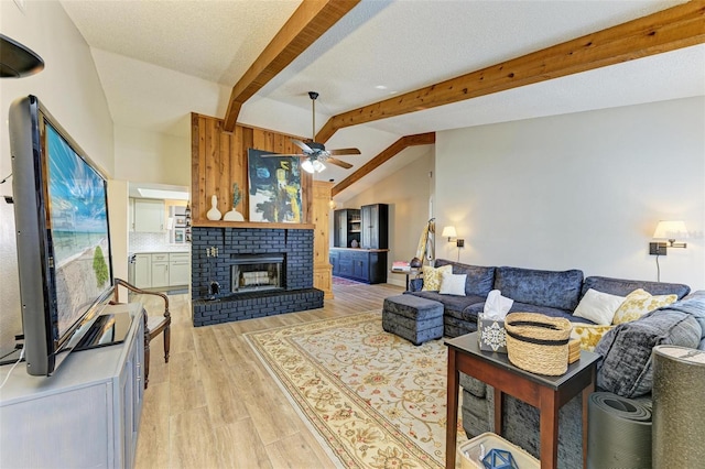 living room with light hardwood / wood-style flooring, ceiling fan, a fireplace, lofted ceiling with beams, and a textured ceiling