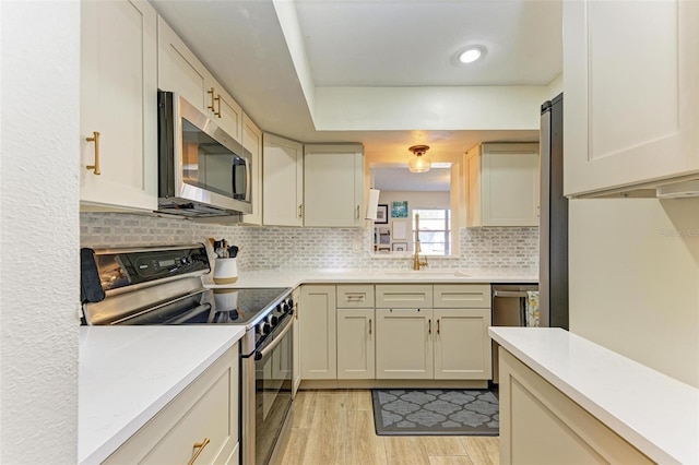 kitchen featuring appliances with stainless steel finishes, sink, backsplash, light hardwood / wood-style floors, and cream cabinets