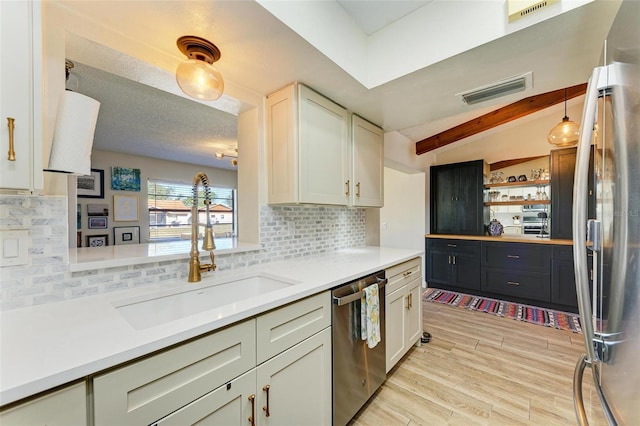 kitchen with pendant lighting, sink, decorative backsplash, stainless steel appliances, and light hardwood / wood-style flooring