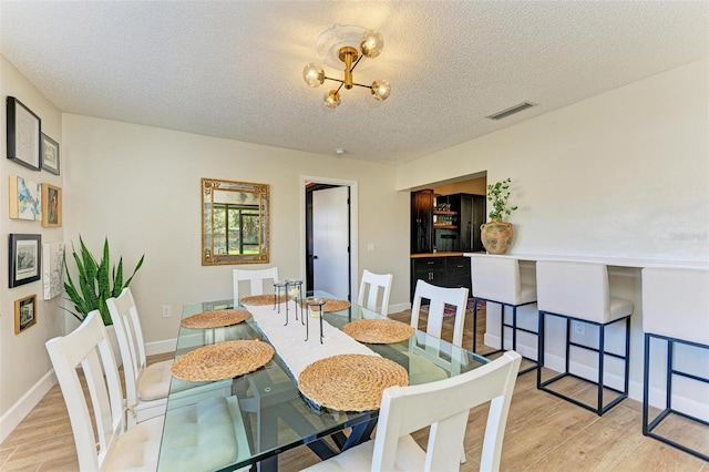 dining room with a chandelier, a textured ceiling, and light wood-type flooring