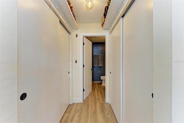 hallway with light hardwood / wood-style floors and a textured ceiling