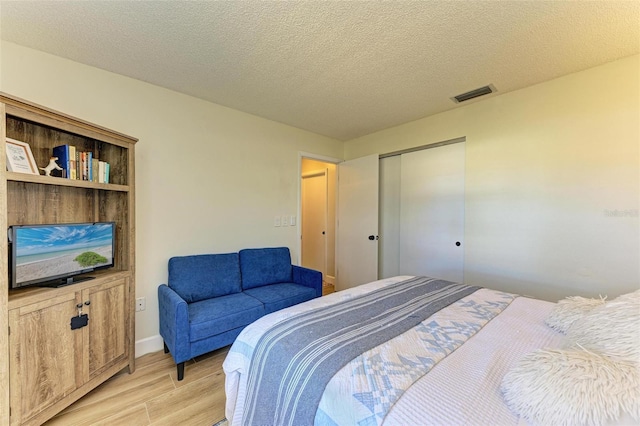 bedroom with light hardwood / wood-style floors, a textured ceiling, and a closet