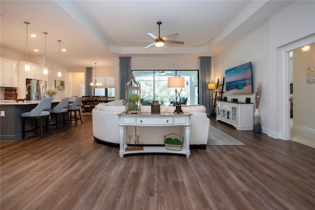 living room with ceiling fan with notable chandelier, dark wood-type flooring, and a raised ceiling