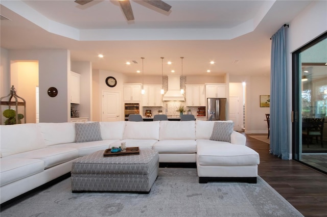 living room with wood-type flooring, a raised ceiling, and ceiling fan