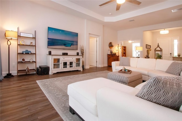 living room with dark wood-type flooring, ceiling fan, and a tray ceiling