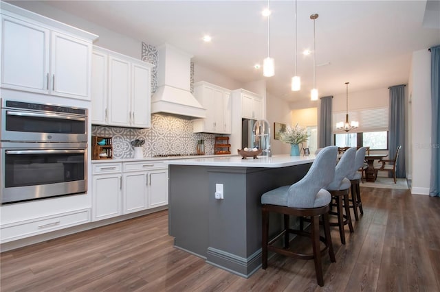 kitchen featuring premium range hood, white cabinetry, stainless steel appliances, and decorative light fixtures