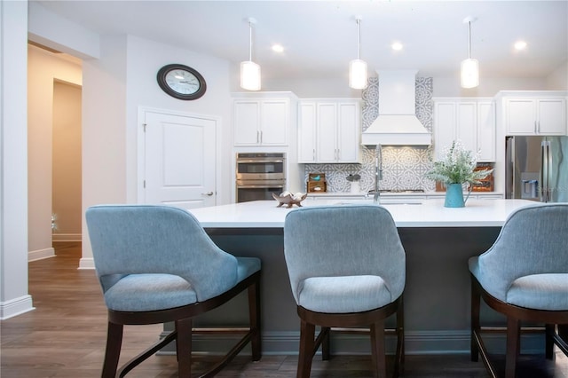 kitchen featuring premium range hood, hanging light fixtures, white cabinets, stainless steel appliances, and backsplash