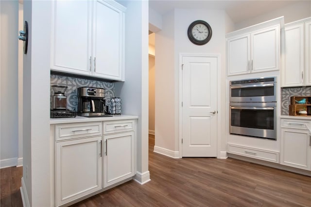 kitchen featuring dark wood-type flooring, double oven, tasteful backsplash, and white cabinets