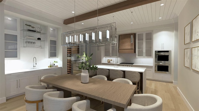 kitchen featuring sink, white cabinetry, hanging light fixtures, beamed ceiling, and stainless steel appliances