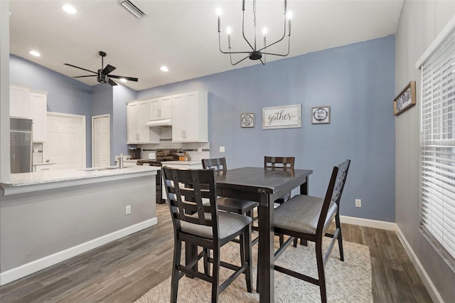 dining space with sink, ceiling fan with notable chandelier, and dark hardwood / wood-style floors