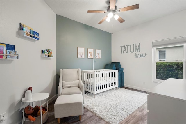 bedroom featuring wood-type flooring, a nursery area, and ceiling fan