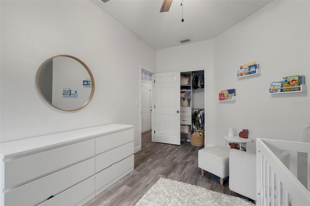 bedroom with dark wood-type flooring, ceiling fan, and a crib