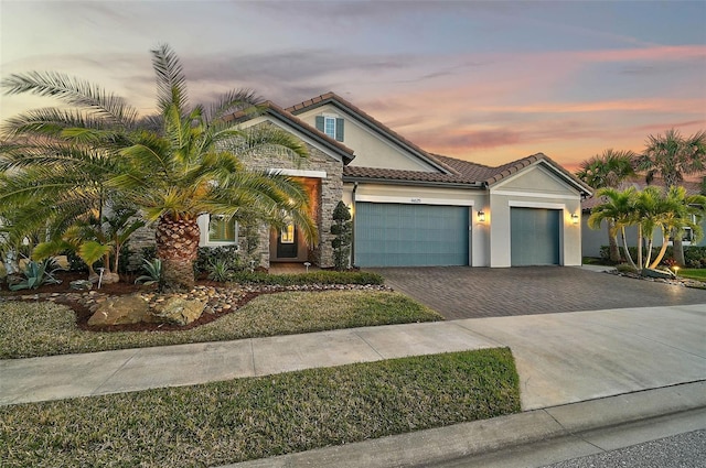 view of front of property featuring a tiled roof, decorative driveway, an attached garage, and stucco siding