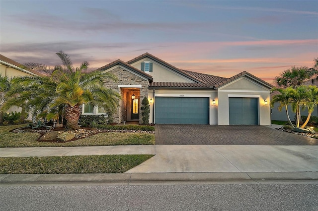 view of front of house with a garage, stone siding, a tile roof, decorative driveway, and stucco siding