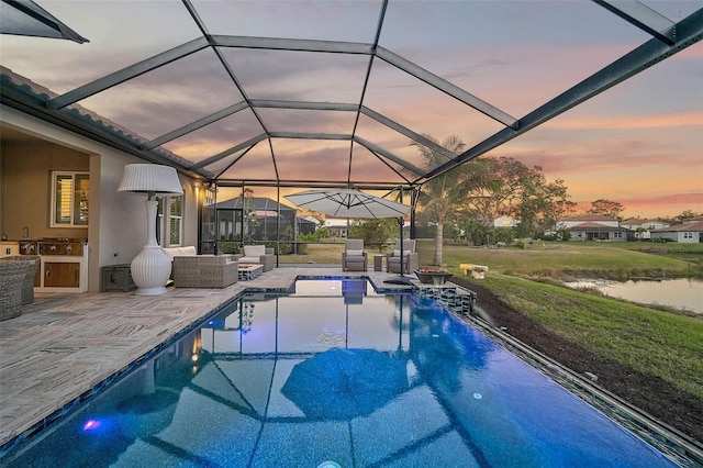 pool featuring glass enclosure, a water view, a patio, and area for grilling