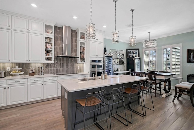 kitchen with decorative backsplash, wall chimney exhaust hood, light wood finished floors, a kitchen bar, and crown molding