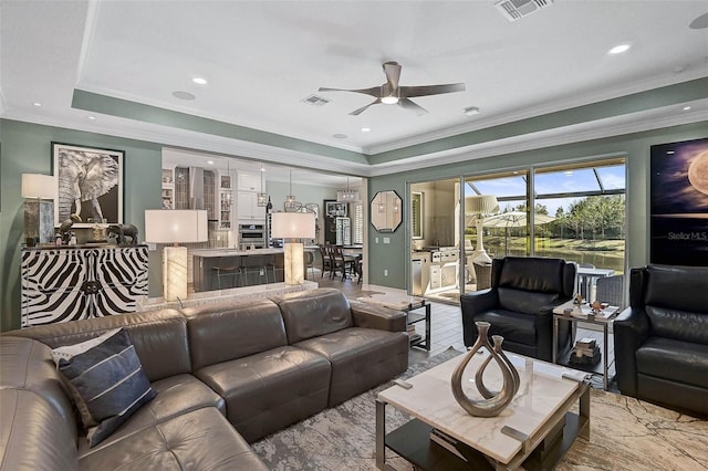 living room featuring ornamental molding, a tray ceiling, visible vents, and a ceiling fan