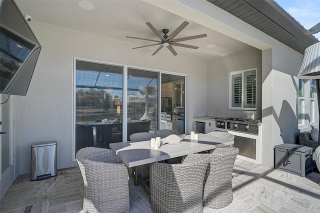 view of patio featuring ceiling fan, exterior kitchen, outdoor dining space, and a sink