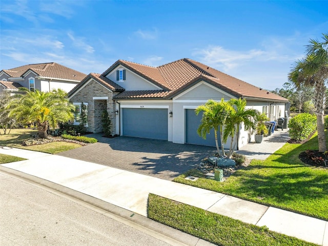 mediterranean / spanish house featuring a garage, a tiled roof, decorative driveway, stucco siding, and a front yard