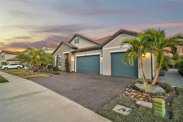 mediterranean / spanish home with a garage, a tiled roof, decorative driveway, and stucco siding