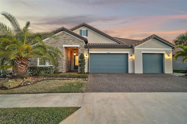 view of front facade with stone siding, a tile roof, an attached garage, decorative driveway, and stucco siding