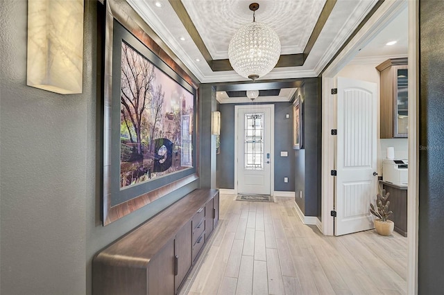 foyer entrance featuring a tray ceiling, crown molding, an inviting chandelier, light wood-style floors, and baseboards