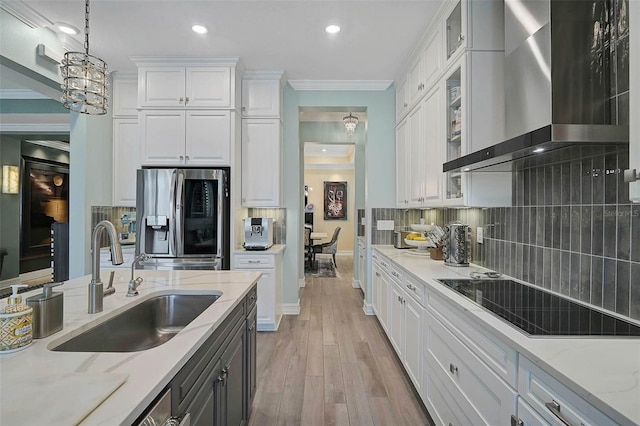 kitchen featuring stainless steel fridge with ice dispenser, wall chimney exhaust hood, black electric cooktop, white cabinetry, and a sink