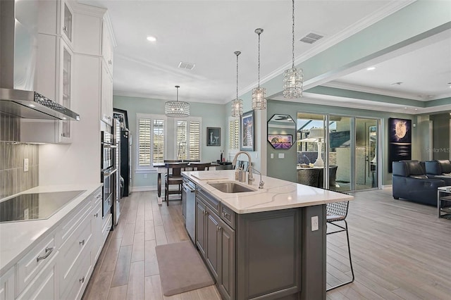 kitchen with wall chimney exhaust hood, a sink, visible vents, and light wood-style floors