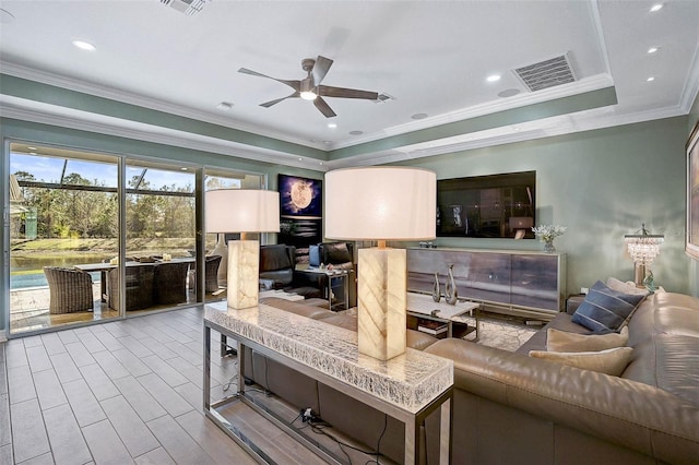 living area with a tray ceiling, visible vents, wood finished floors, and ornamental molding