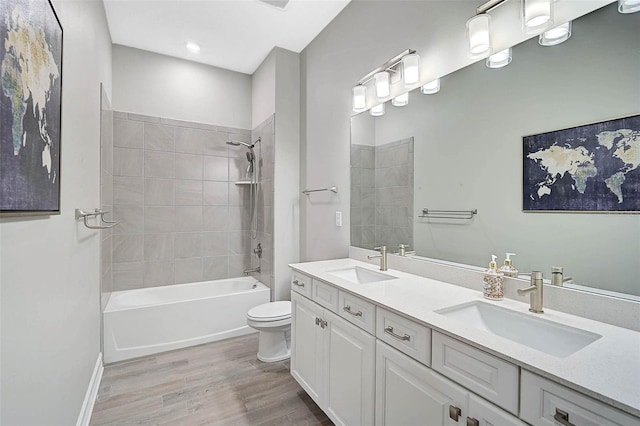 full bathroom with toilet, double vanity, a sink, and wood finished floors