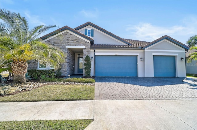 ranch-style house with decorative driveway, stucco siding, a garage, stone siding, and a tiled roof