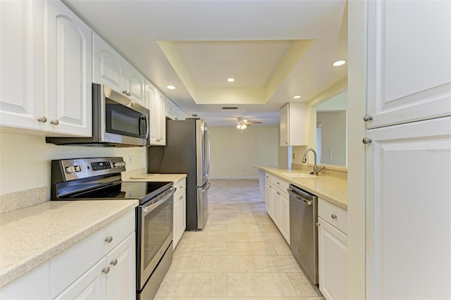 kitchen with sink, ceiling fan, white cabinetry, stainless steel appliances, and a tray ceiling