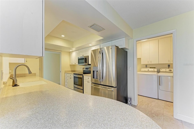 kitchen featuring sink, appliances with stainless steel finishes, independent washer and dryer, a tray ceiling, and white cabinets