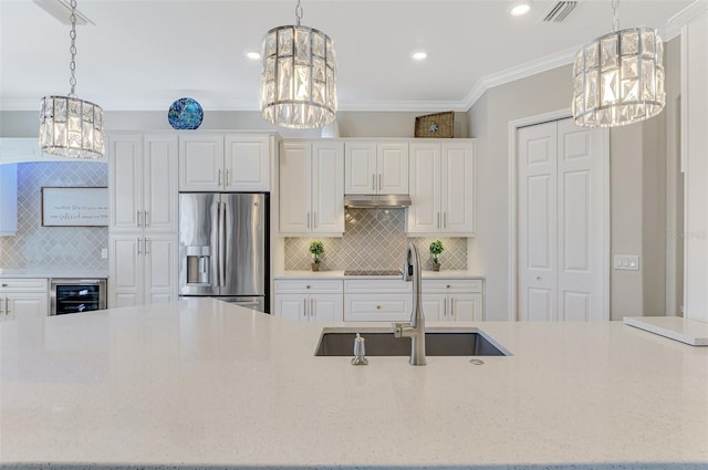 kitchen with sink, stainless steel fridge, light stone counters, ornamental molding, and beverage cooler