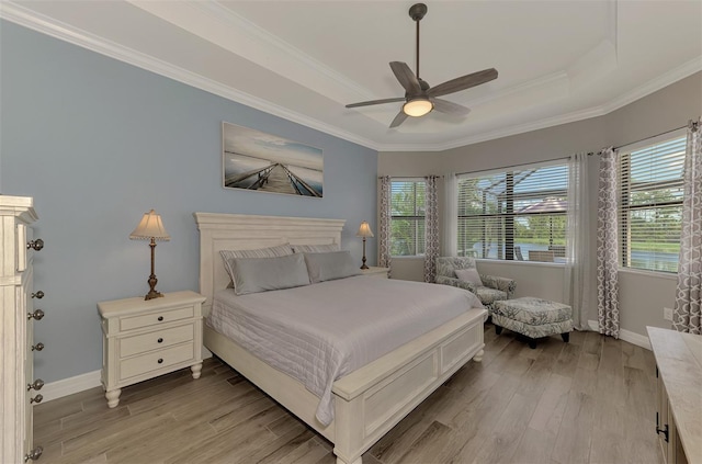 bedroom featuring crown molding, ceiling fan, a tray ceiling, and light hardwood / wood-style flooring